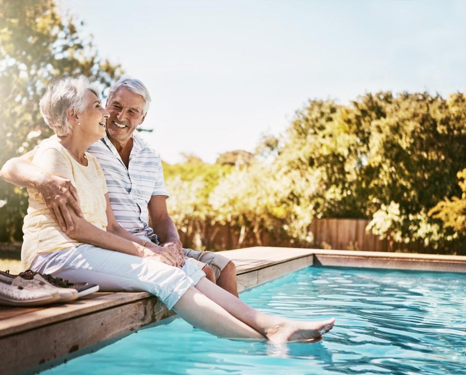 Smiling couple sitting on the edge of a pool.