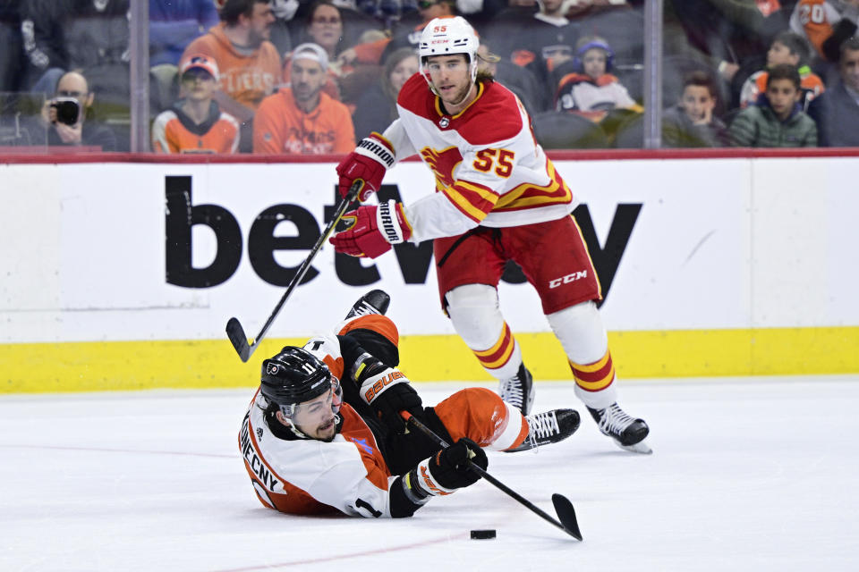 Philadelphia Flyers' Travis Konecny, bottom, plays the puck past the defense of Calgary Flames' Noah Hanifin during the second period of an NHL hockey game, Saturday, Jan. 6, 2024, in Philadelphia. (AP Photo/Derik Hamilton)