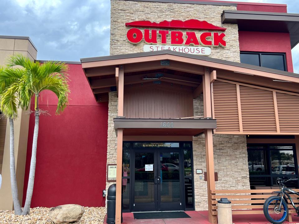 Outback Steakhouse exterior with wood panels, red walls, and tree out front