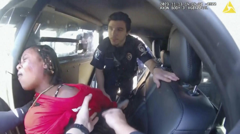 This image made from video provided by the Charlotte-Mecklenburg, N.C., Police Department shows officers attempting to put a woman in the back of a police car after arresting her. On Tuesday, Dec. 12, 2023, police released the video from the arrest in North Carolina last month, showing that before an officer repeatedly punched a Black woman while others held her down, the woman struck an officer in the face and he responded by hitting her back and knocking her off her feet. (Charlotte-Mecklenburg Police Department via AP)