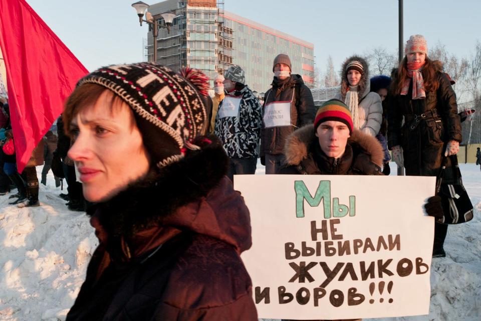 A protester wearing a hat stands in front of a sign in Russian that translates to 'We did not vote for crooks and thieves!'