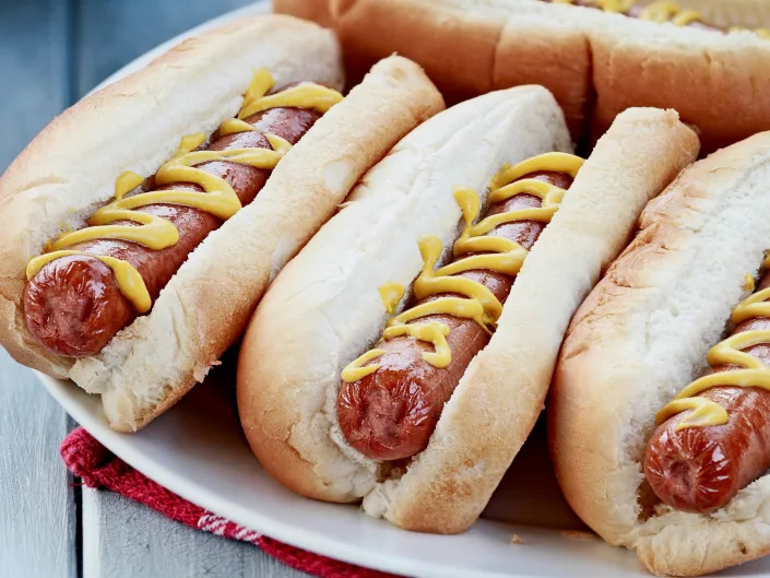 Three hot dogs in a bun with mustard.