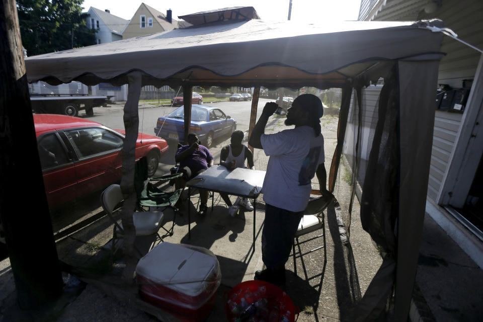 FILE - In this Wednesday, July 4, 2012 file photo, Dave Bailey, right, gulps water from a bottle while hanging inside of a tent on the sidewalk with his sons Daquan Bailey, 14, left, and Davandre Bailey, 17, while beating the heat on Fourth of July in Paterson, N.J. According to a study published Tuesday, May 25, 2021 in Nature Communications, during the summer of 2017 in nearly all large urban areas, people of color are exposed to more extreme urban heat than white people. (AP Photo/Julio Cortez, File)
