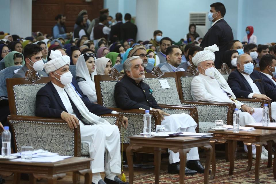 The Afghan president, several other government officials and the Afghan public sit listening in a large assembly, wearing masks