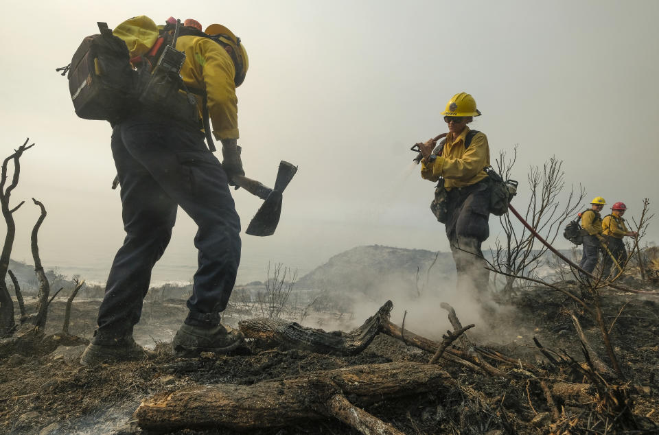 County of Santa Barbara Fire Departement firefighters extinguish a roadside fire off off the U.S. 101 highway Wednesday, Oct. 13, 2021, in Goleta, Calif. A wildfire raging through Southern California coastal mountains threatened ranches and rural homes and kept a major highway shut down Wednesday as the fire-scarred state faced a new round of dry winds that raise risk of flames. (AP Photo/Ringo H.W. Chiu)