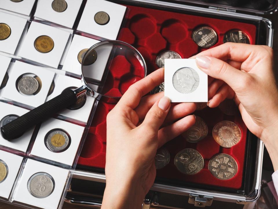 A box with collectible coins in cells and a hand holding a coin. According to a May YouGov poll of nearly 3,000 American adults, over 80 percent reported they would stop to pick up coins on the street, with the habit being common among older adults. (Getty Images/iStockphoto)