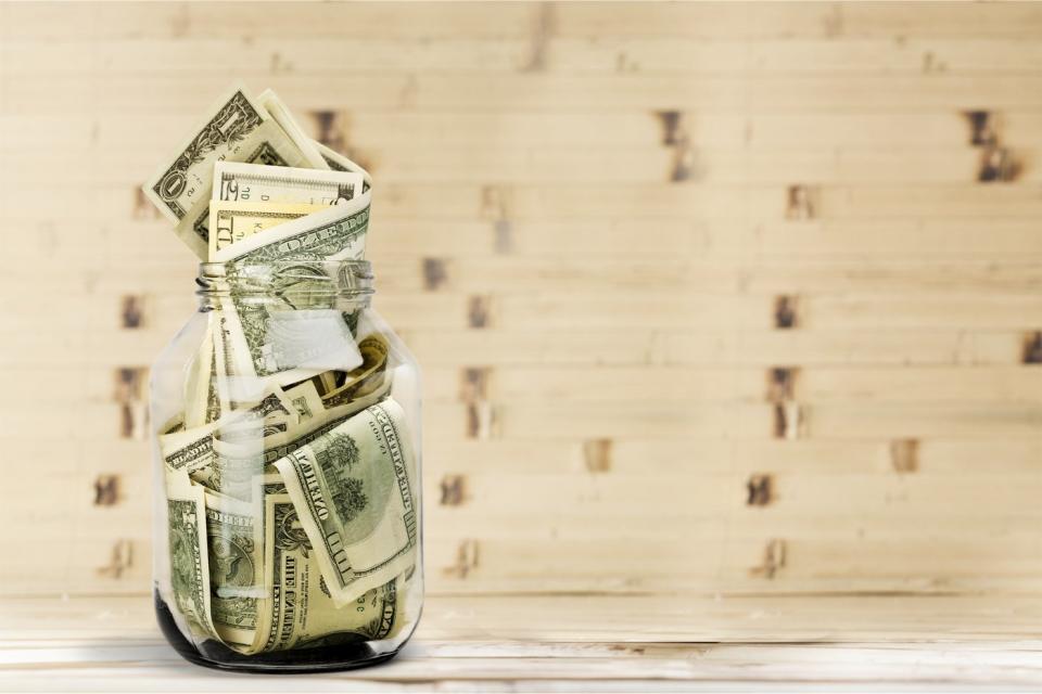 A glass jar full of dollar bills on a wooden table.