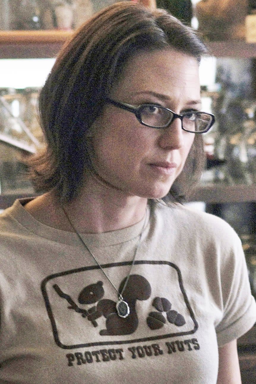 A woman wearing glasses and a t-shirt talking to a man in a diner. Various jars and kitchen items are on shelves behind them