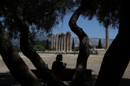 A tourist sits under the shadow of a tree during a hot day, at the archaeological site of the Temple of Zeus in Athens