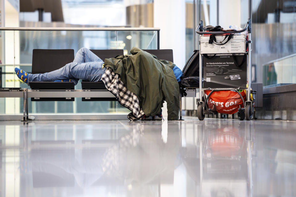 A person sleeps on a bench in the departure hall at Munich Airport, Germany, Wednesday, Jan. 17, 2024. Heavy snowfalls and freezing rain across Germany Wednesday led to the cancellation of hundreds of flights and trains, crashes on icy roads, and school closures. (Matthias Balk/dpa via AP)