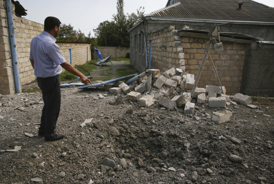 A man points to a crater that was allegedly caused by shelling during fighting over the breakaway region of Nagorno-Karabakh, in Tartar region, Azerbaijan, Wednesday, Sept. 30, 2020. Leaders of Azerbaijan and Armenia brushed off the suggestion of peace talks Tuesday, accusing each other of obstructing negotiations over the separatist territory of Nagorno-Karabakh, with dozens killed and injured in three days of heavy fighting. (AP Photo/Aziz Karimov)