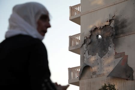 A woman stands in front of an apartment building which was damaged by a rocket fired from Syria, in Nusaybin