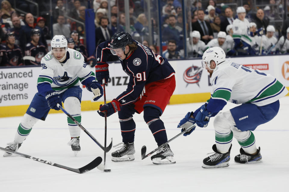 Columbus Blue Jackets' Kent Johnson, center, carries the puck across the blue line between Vancouver Canucks' Ilya Mikheyev, left, and Filip Hronek during the second period of an NHL hockey game Monday, Jan. 15, 2024, in Columbus, Ohio. (AP Photo/Jay LaPrete)