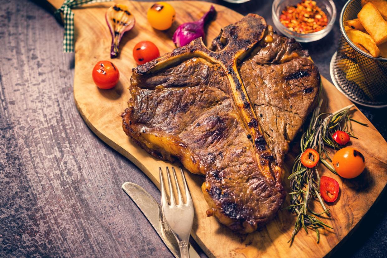 Top view of medium roasted t-bone steak with french fries,roasted cherry tomatoes,red chili peppers,spices and glass of red wine over dark rustic background.