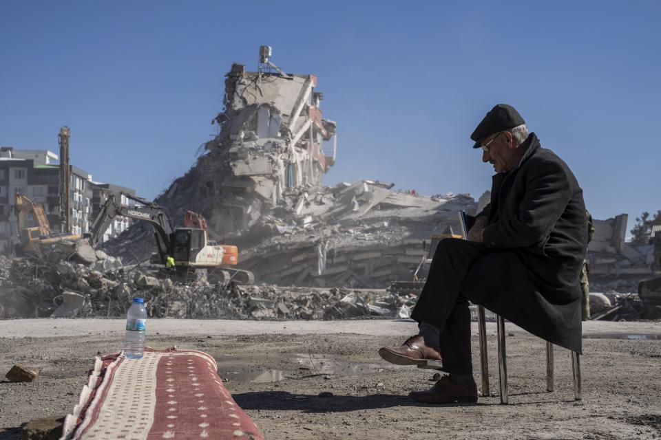 Mehmet Nasir Duran, 67, sits on a chair, as heavy machines remove debris from a building, where five of his family members are trapped in Nurdagi, southeastern Turkey, Thursday, Feb. 9, 2023.Thousands who lost their homes in a catastrophic earthquake huddled around campfires and clamored for food and water in the bitter cold, three days after the temblor and series of aftershocks hit Turkey and Syria. (AP Photo/Petros Giannakouris)