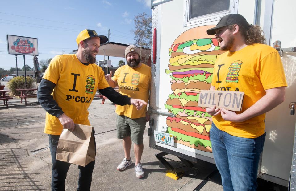 From left, Brown Bagger food truck co-owners Tim Thompson and Ellis O'Neal have a laugh with Gulf Coast Garage Patio Bar owner Austin Leek as he holds a makeshift "Milton" sign over the "P'Cola" on his shirt in downtown Milton on Tuesday, Jan. 9, 2024. Brown Bagger is opening this second food truck at the Gulf Coast Garage Patio Bar in the near future.