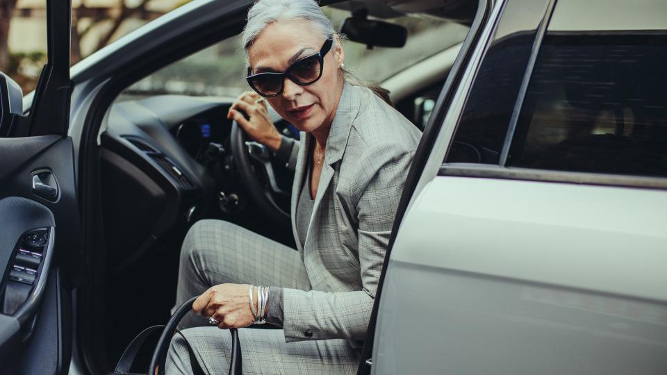 Senior businesswoman with purse getting out of her car.