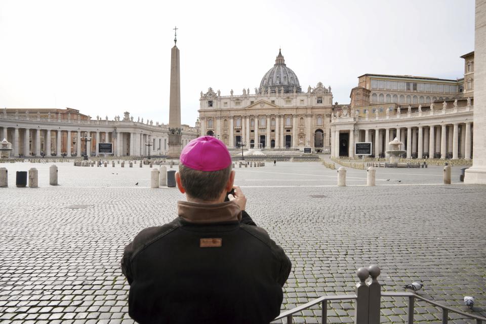 A prelate takes a photograph of an empty St Peter's Square at the Vatican in Rome.