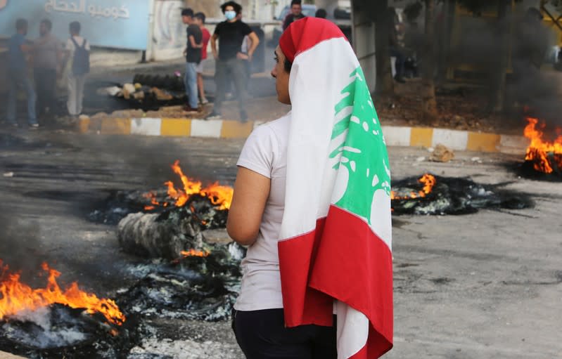 A demonstrator wearing a Lebanese flag stands near burning tires during a protest in Nabatiyeh