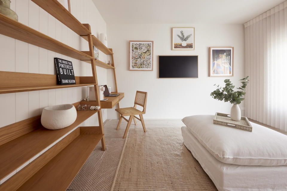 Shelves and a chair on the left, pictures on the back wall and an ottoman on the right. 