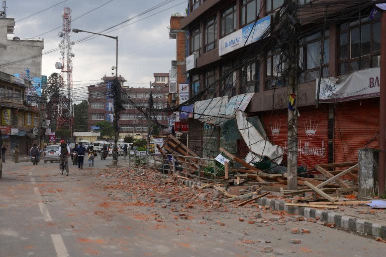 Nepalese people walk past a collapsed building in Kathmandu, on April 25, 2015