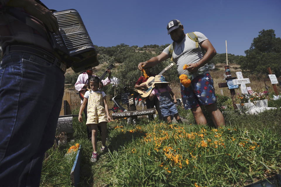 With a musician playing and accompanied by his family, Masiel Ventura places flower petals on the tomb of his brother-in-law in the Valle de Chalco municipal cemetery as people begin to arrive to pay their respects to their dead, on the outskirts of Mexico City, Sunday, Oct. 31. 2021. (AP Photo/Marco Ugarte)