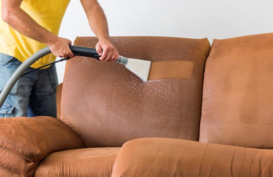 Person using vacuum attachment to deep clean a couch
