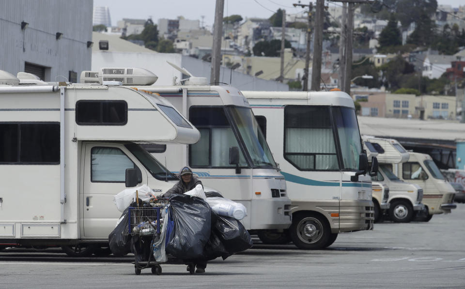 FILE - In this Thursday, June 27, 2019, file photo a homeless person pushes a cart past parked RVs along a street in San Francisco. San Franciscans should put aside their political differences and support finding homes for more than 1,000 homeless people, according to a public engagement campaign beginning Thursday, July 25, 2019. (AP Photo/Jeff Chiu, File)