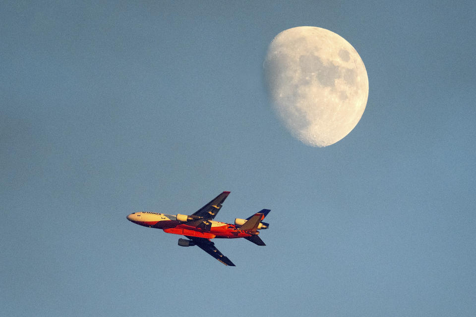 An air tanker battling the Windy Fire flies the moon in the background Thursday, Sept. 16, 2021, on the Tule River Reservation in California. (AP Photo/Noah Berger)