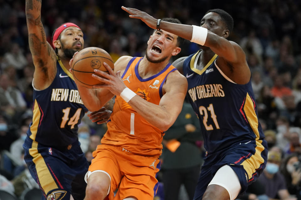 Phoenix Suns guard Devin Booker (1) drives as New Orleans Pelicans forward Brandon Ingram (14) and forward Tony Snell (21) defend during the second half of an NBA basketball game, Friday, Feb. 25, 2022, in Phoenix. (AP Photo/Matt York)