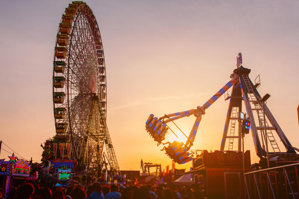 Ferris wheel and swinging ride at an amusement park during sunset. Crowds of people are seen enjoying the fairground attractions