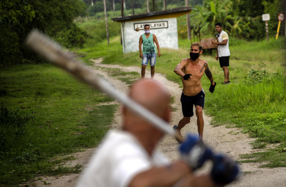 En esta imagen, tomada el 27 de mayo de 2020, un grupo de residentes, con mascarilla para protegerse del coronavirus, juegan al béisbol en el vecindario de Las Playas, en el este de La Habana, Cuba. Las autoridades cubanas exigen el uso de mascarilla para salir de casa. (AP Foto/Ramón Espinosa)