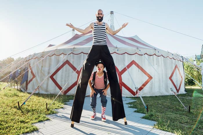Circus performer on stilts posing outside the tent with another performer between their legs