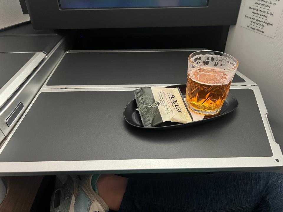 A beer and nuts on a plate on the tray table.