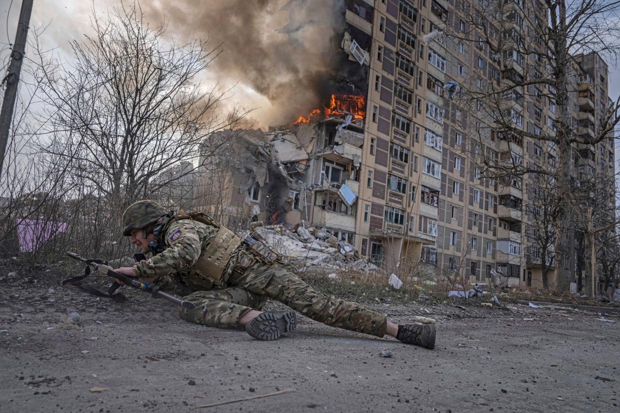 A Ukrainian police officer takes cover in front of a burning building that was hit in a Russian airstrike in Avdiivka on 17 March (AP)