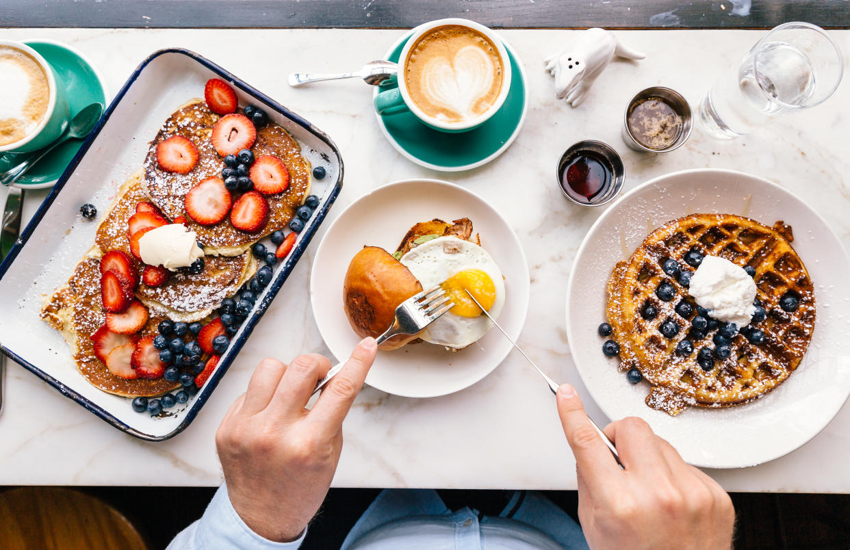 Breakfast foods on a table, including pancakes, waffles and eggs on a roll.