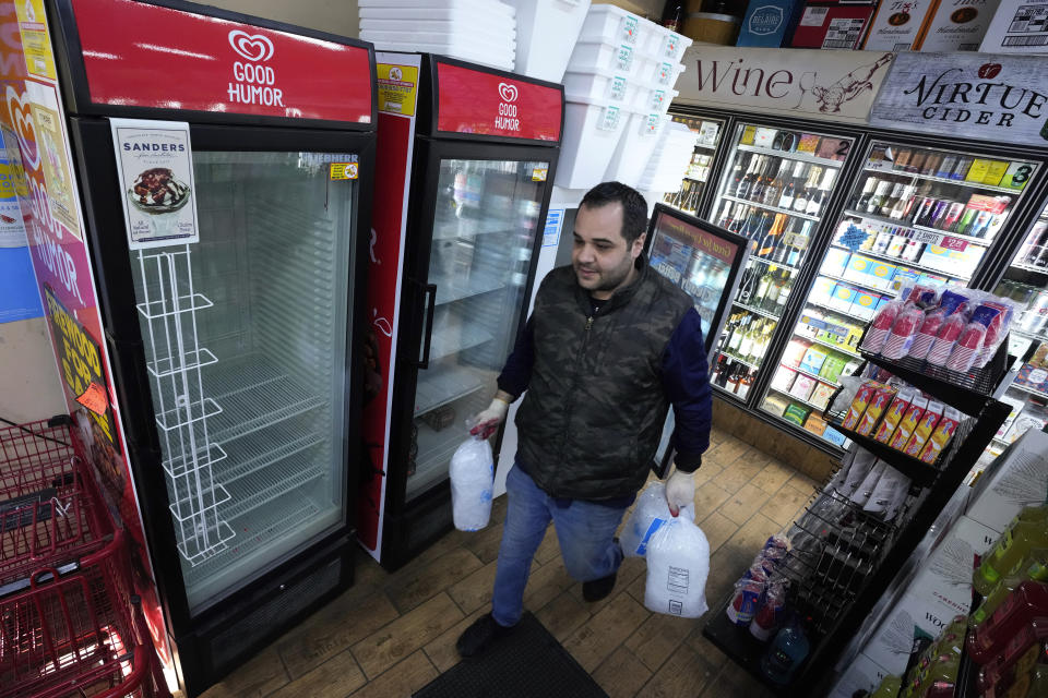 Kevin Savaya, manager at Mr. C's Deli, carries bags of ice past empty coolers in Grosse Pointe Farms, Mich., Friday, Feb. 24, 2023. The business was staying open using a generator. Michigan is shivering through extended power outages caused by one of the worst ice storms in decades. (AP Photo/Paul Sancya)