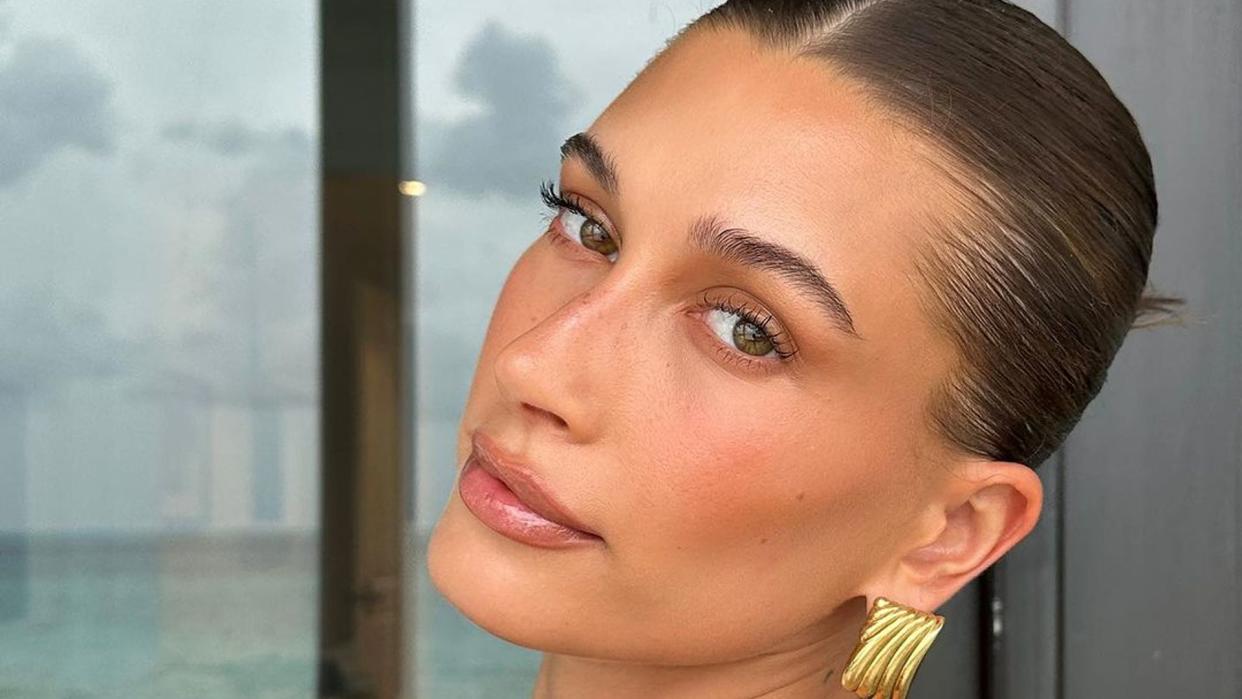 Hailey Bieber looks at camera with her hair up and wearing gold earring