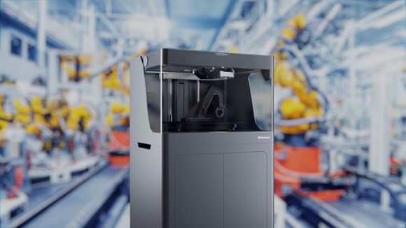 A Markforged X5 composite 3D printer with an out-of-focus view of a factory in the background.