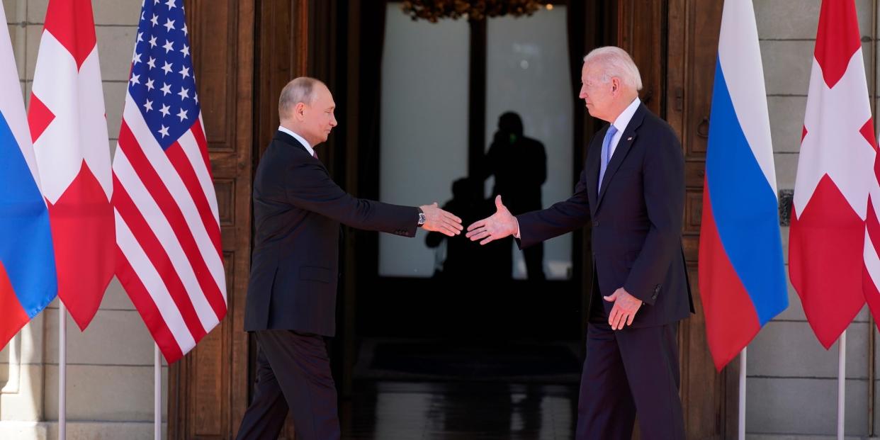Vladimir Putin and Joe Biden reach to shake hands.