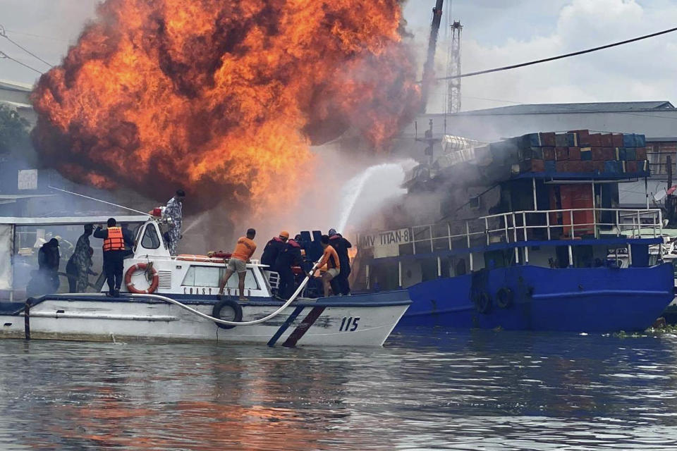 In this photo provided by the Philippine Coast Guard, members of the Philippine Coast Guard try to extinguish flames on a burning cargo ship docked in Manila, Philippines, Saturday, June 12, 2021. The fire and a powerful blast ripped through ship docked to refuel in the Philippine capital of Manila on Saturday, injuring at least six people and igniting a blaze in a nearby riverside slum that gutted dozens of shanties, officials said. (Philippine Coast Guard via AP)