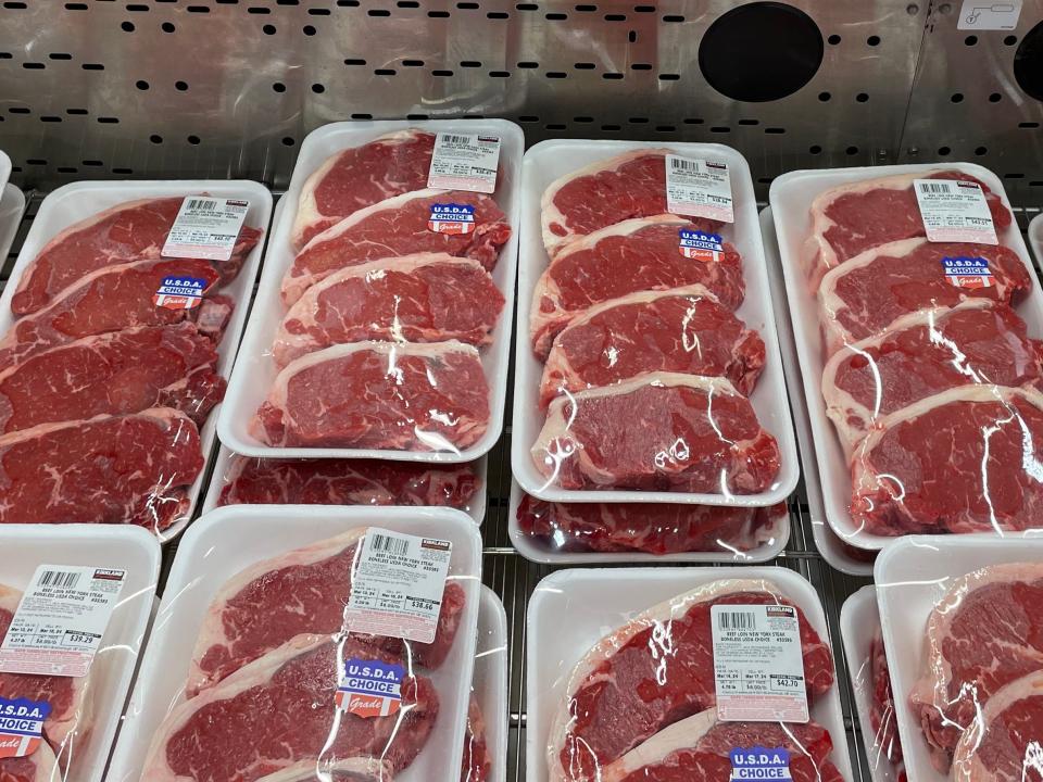 Plastic trays of beef loin New York steak in refrigerated section at Costco. Most trays contain four loins each