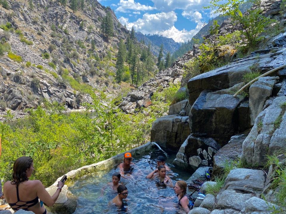 Group of people in a stone hot tub at the edge of stone mountains