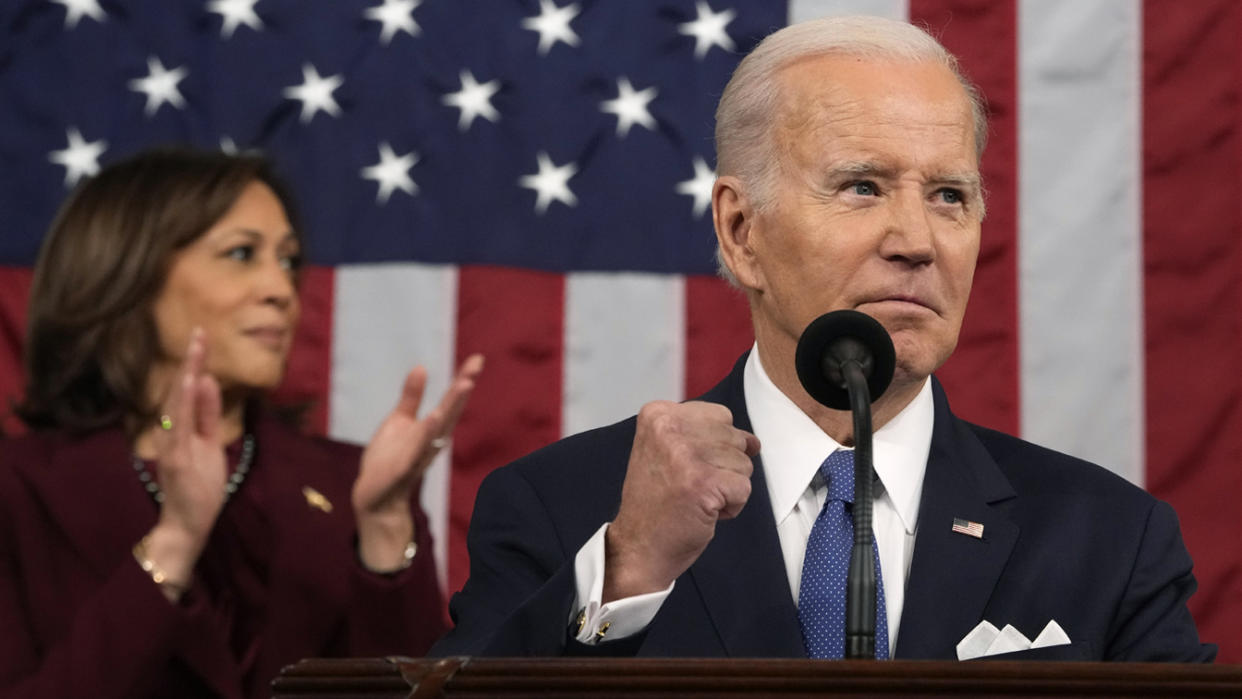 President Biden holds a up fist at a podium in front of an American flag, while Kamala Harris applauds behind him.