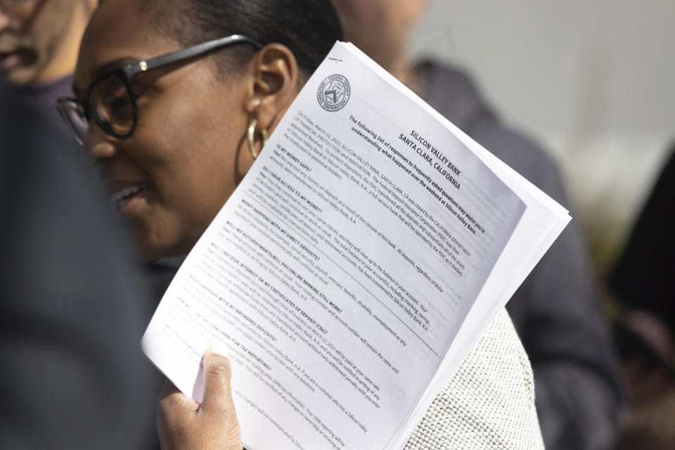 FDIC member Dedra Dorn distributes "frequently asked questions" hand outs to individuals at the Silicon Valley Bank's headquarters in Santa Clara, Calif., on Monday, March 13, 2023. The federal government intervened Sunday to secure funds for depositors to withdraw from Silicon Valley Bank after the banks collapse. Dozens of individuals waited in line outside the bank to withdraw funds. (AP Photo/ Benjamin Fanjoy)