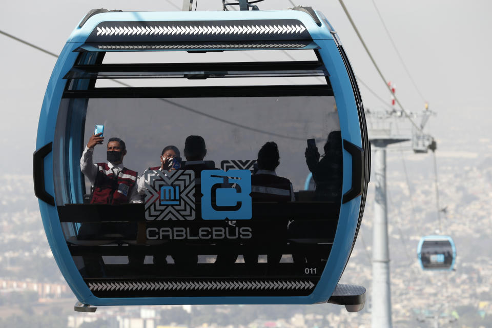 Officials take pictures as they ride in a cable car between the Campos Revolucion and Tlalpexco stations, during the inauguration of a new aerial public transit system dubbed the Cablebus, in the Cuautepec neighborhood of northern Mexico City, Thursday, March 4, 2021. For the residents of Cuautepec, this new system, the first of four planned lines, will turn a commute to the nearest subway station, that can last up to two hours, into a 30-minute ride. (AP Photo/Rebecca Blackwell)