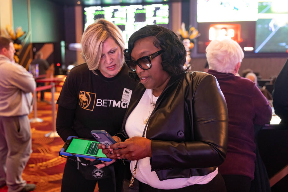 A BetMGM employee, left, helps Adrienne Williams of Garfield Heights set up a sports betting app on her smartphone.