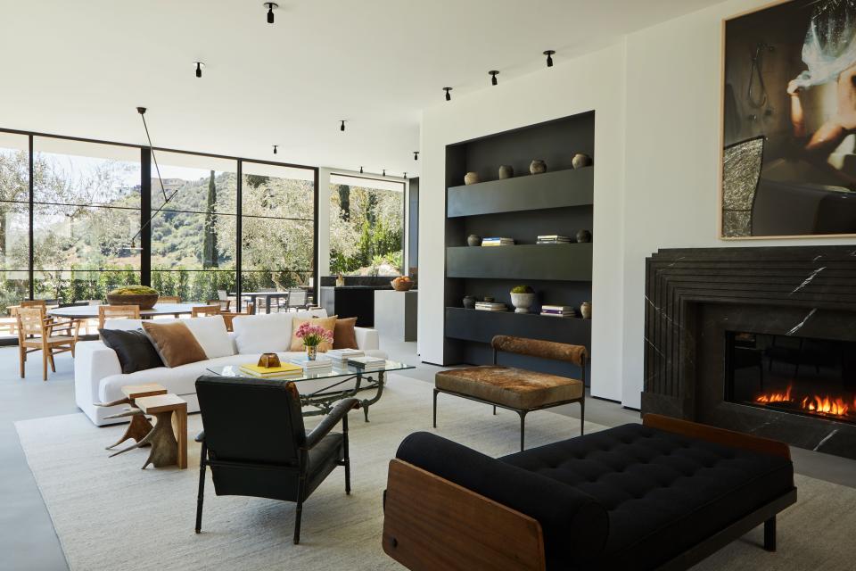 In the main living space, the Jean Prouvé S.C.A.L. metal and wood daybed (circa 1950) combines with a Jacques Adnet leather chair (from the 1960s). Both the Stag T stools and the brown Alchemy bench from Carpenters Workshop Gallery are by Rick Owens. The photograph above the fireplace is by Kerry Skarbakka and the silver wool Soumak rug is from Lawrence of La Brea.