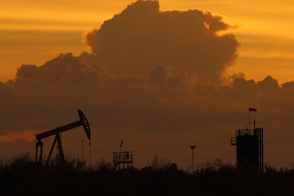 The silhouette of an oil pump at dusk with clouds in the background.