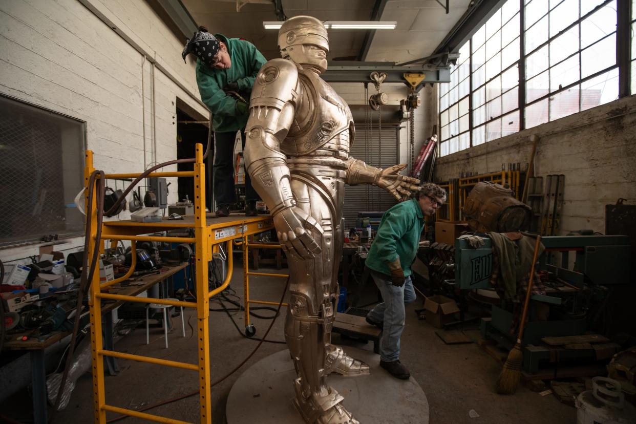 Nadine Chronopoulos, left, works on the grinding and sanding of an 11-foot RoboCop statue at a warehouse on Detroit's east side on Feb. 24, 2021, while finishing the statue before patina being applied as Jay Jurma walks around the statue. The statue will be housed somewhere while waiting for a home to be announced.